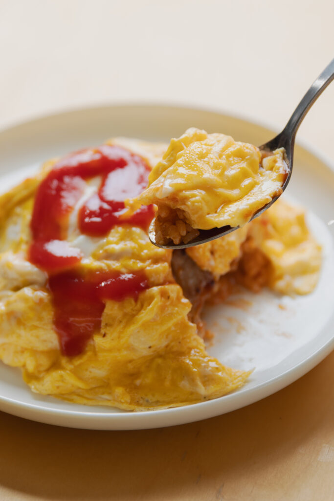 Homemade Japanese omurice chicken rice bowl topped with a fluffy runny omelet and ketchup