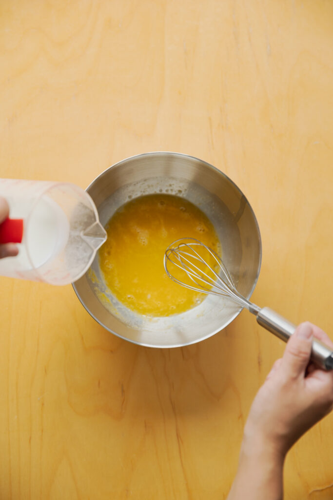 Pouring milk into whisked egg and sugar in a stainless steel bowl for Japanese custard pudding