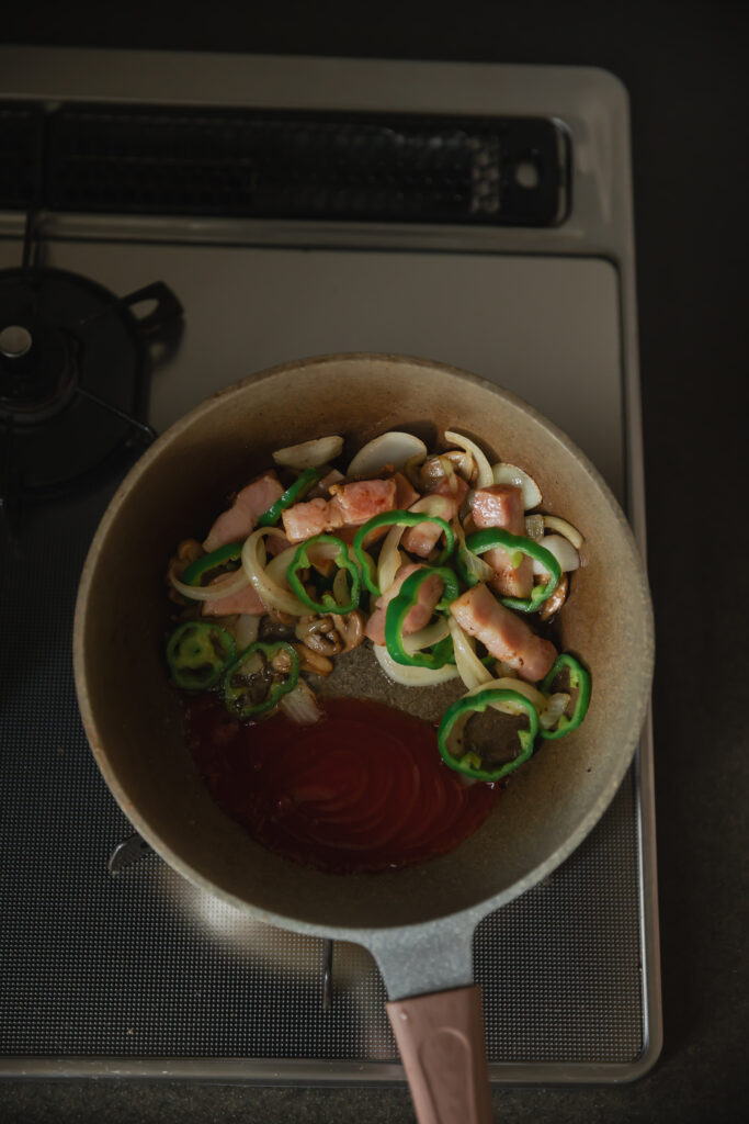 Pan-frying thick bacon slices, onions, and green bell peppers with tomato ketchup in a pan for Japanese Napolitan
