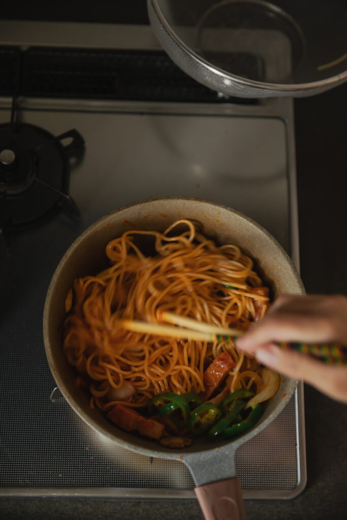 Stir-frying spaghetti noodles with rich red tomato sauce and vegetables using chopsticks