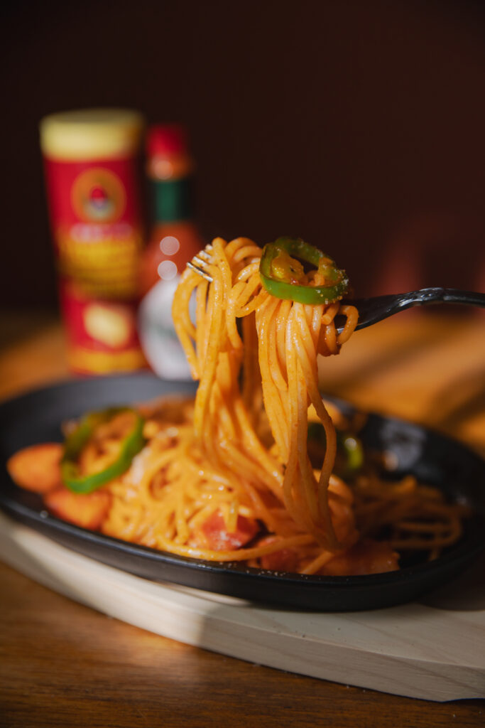 A fork twirling a bite of shiny Japanese ketchup pasta Napolitan showing rich glazes and textures