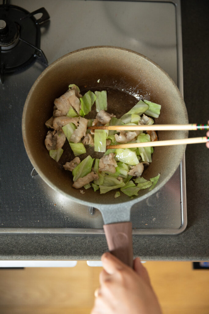 Stir-frying pork slices and cabbage in a pan with chopsticks for Japanese yakisoba