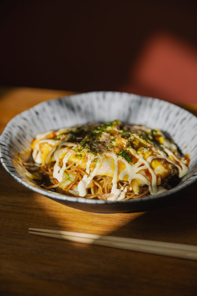 Authentic Japanese Omu-Yakisoba with fluffy egg omelet wrapper topped with sweet sauce and mayonnaise drizzle on a premium ceramic plate