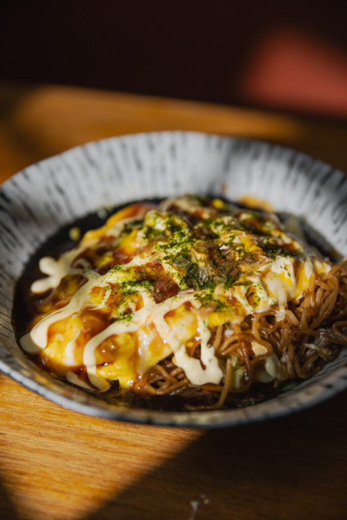 Close-up shot of glossy, savory Omu-Yakisoba under perfect lighting showing rich mayonnaise lattices and green seaweed flakes