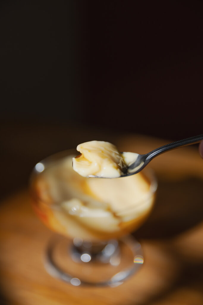 A spoon scooping a bite of melting, velvety soft Japanese custard pudding with dripping caramel syrup
