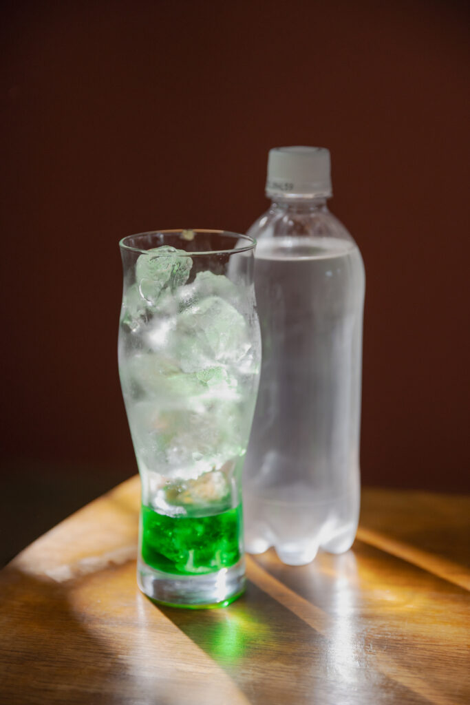 Pouring sparkling water into a glass cup with green melon syrup and ice cubes for Japanese melon soda