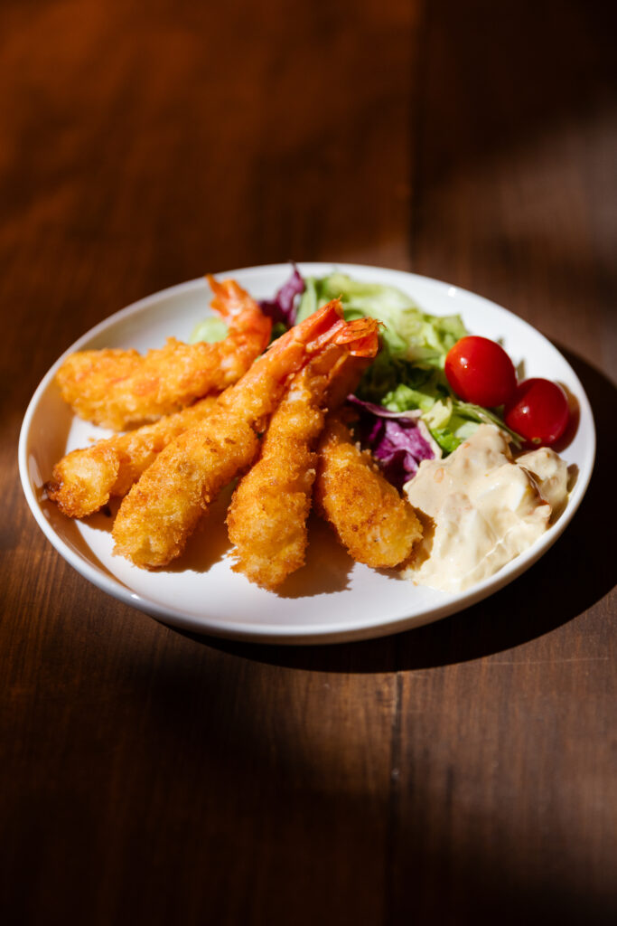 A plate of golden brown crispy Japanese Ebi Fry served with shredded cabbage, cherry tomatoes, and creamy tartar sauce under dramatic spotlight