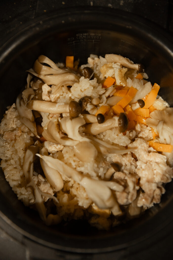 Opening a Japanese rice cooker filled with freshly steamed hot chicken mushroom takikomi gohan rice with steam rising