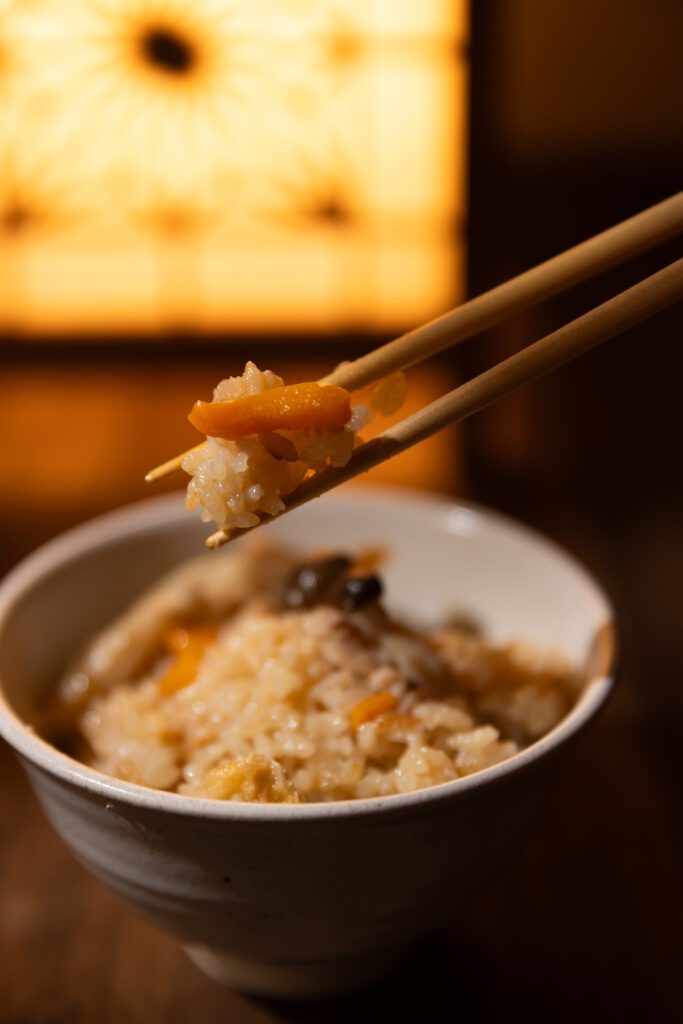Chopsticks lifting a mouthful of savory Japanese chicken mushroom rice with carrots under beautiful warm spotlight