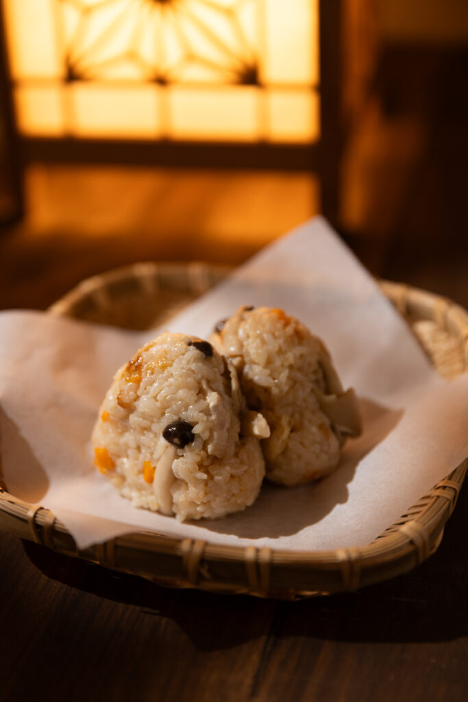 Two rustic Japanese chicken mushroom takikomi gohan onigiri rice balls placed inside a traditional woven bamboo basket