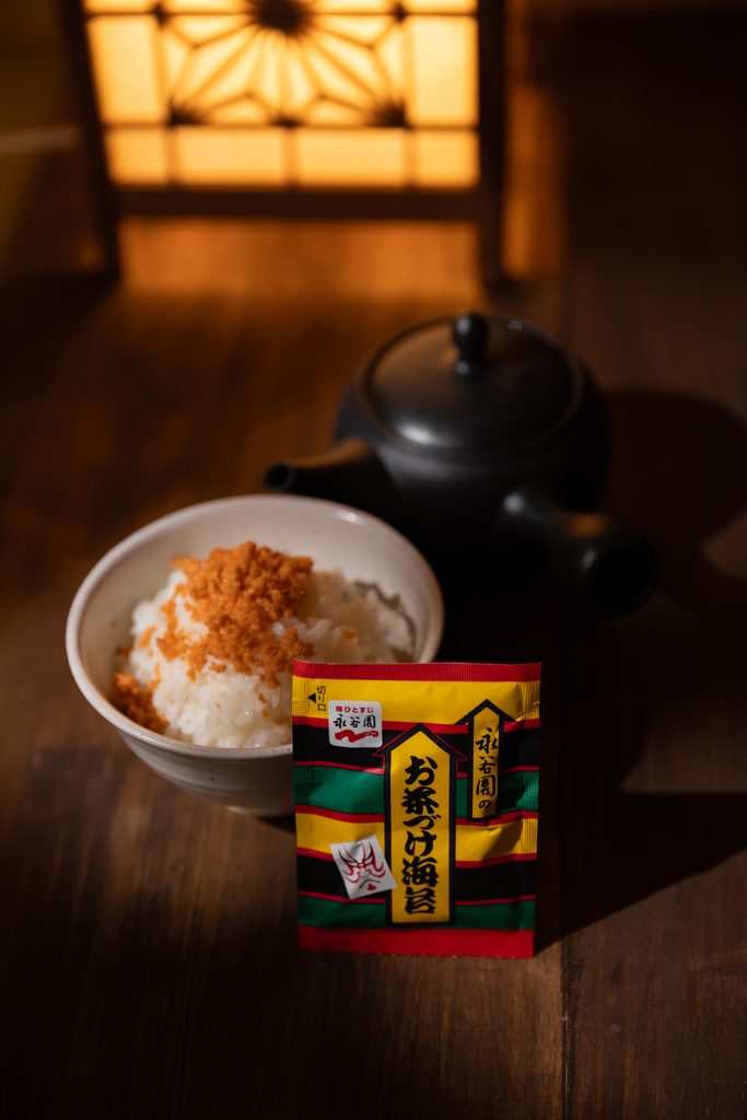 A packet of instant Japanese ochazuke seasoning in front of a bowl of salmon rice and a black teapot