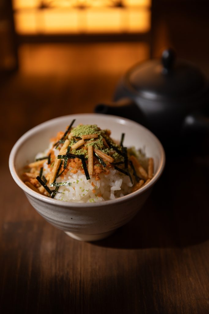 A bowl of Japanese rice topped with flaked salmon, seaweed nori strips, and green tea seasoning pearls