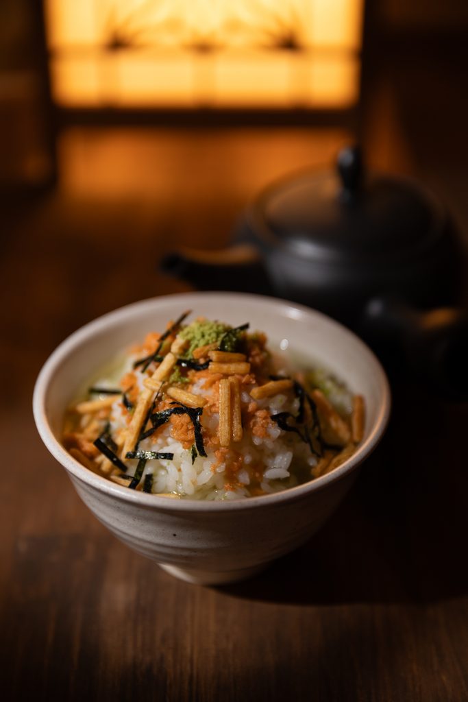 A bowl of Japanese rice topped with flaked salmon, seaweed nori strips, and green tea seasoning pearls