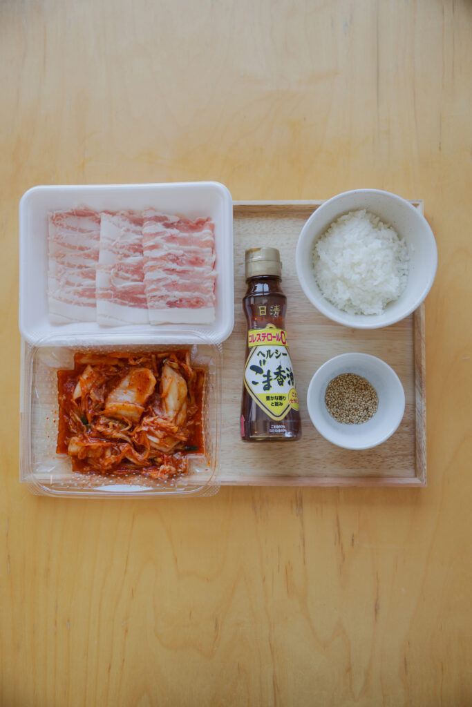 Spicy Korean kimchi in a small ceramic bowl next to a bottle of roasted sesame oil