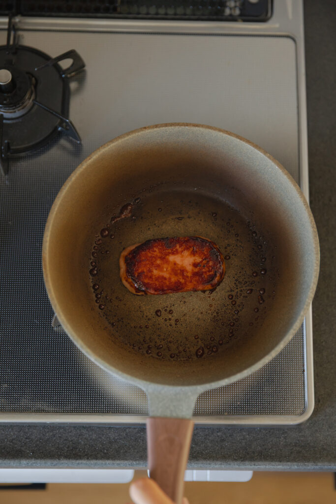 Pan-searing a savory thick slice of Spam in a hot green skillet for Hawaiian style Spam musubi