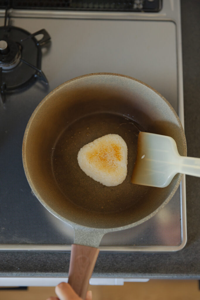 Toasting a triangle yaki-onigiri rice ball in a frying pan using a spatula