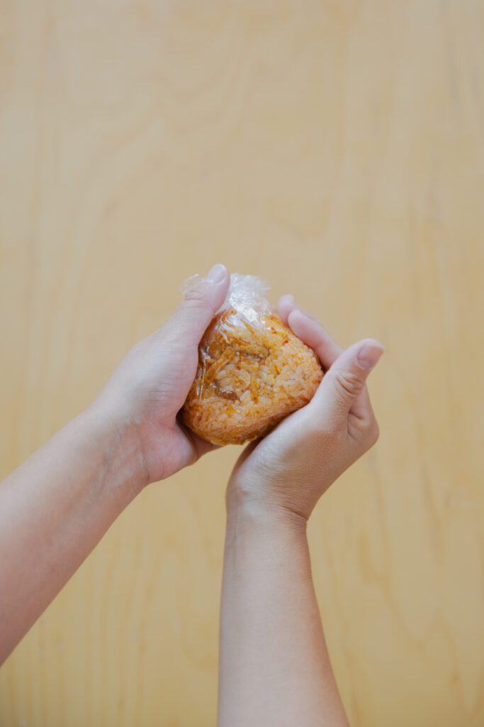 Hand-molding a vibrant orange kimchi pork fried rice onigiri in kitchen