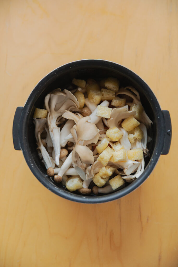 Opening a Japanese rice cooker filled with freshly steamed hot chicken mushroom takikomi gohan rice with steam rising