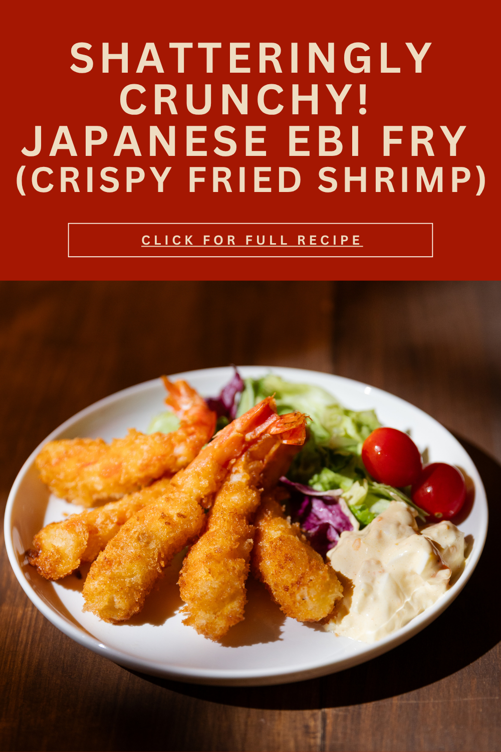A hand lifting a single golden crispy Ebi Fry shrimp by its red tail showing incredible texture under warm light